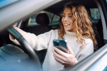 Portrait of a young woman texting on her smartphone while driving a car. Car sharing, rental...