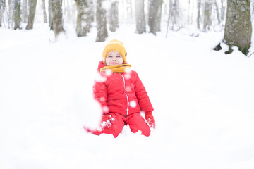 Fototapeta na wymiar Cute little girl in pink snowsuit plays with snow in winter forest