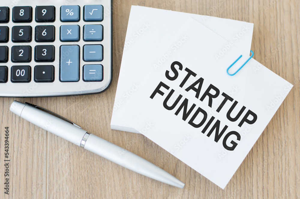 Poster startup funding text on a card on a paper clip to a stack of cards on the table next to the pen and 