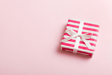 Fototapeta premium wrapped Christmas or other holiday handmade gift box in color paper with ribbon on colored background. Present box, decoration of gift on colored table, top view with copy space