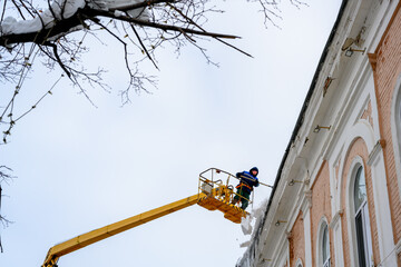 Cleaning icicles and snow from the roof of the house using a lift. Prevention of unsafe situations...