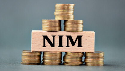 NIM - word on a wooden bar against the background of stacks of coins