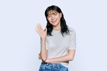 Friendly young woman waving hand in greeting, over white background