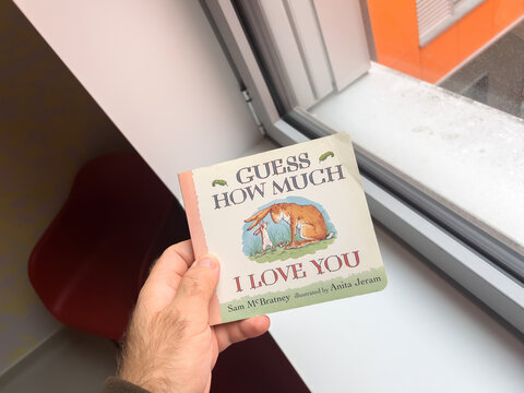 Paris, France - Oct 20, 2022: POV male hand holding book Guess how much I love you near a window sill written by Sam McBartney and illustrated by Anita Jeram