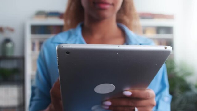 Close-up electronic tablet in hands African American woman student using gadget to visit university website or download educational apps to prepare for college exams stands in room with bookcase - Powered by Adobe