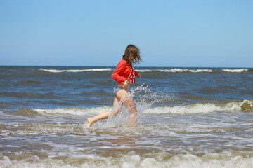 Young woman in bikini and red hoodie running on the beach on beautiful sunny summer day