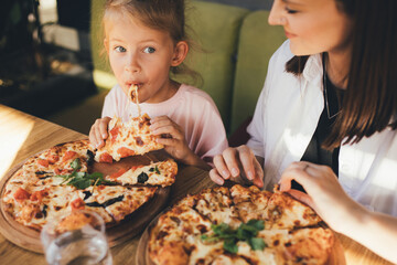 Mother and daughter eat pizza in a cafe.