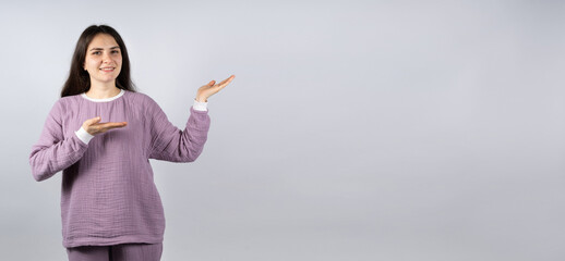 Beautiful brunette woman in comfortable muslin pajamas of lavender color shows her hands to the...