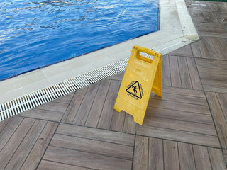 Yellow sign wet floor near the pool with water for swimming and relaxation in a hotel in a warm...