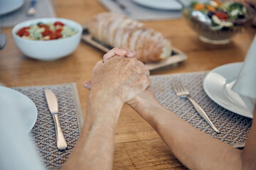 Family, food and prayer with senior couple holding hands, paying and gratitude at dining table for...