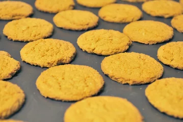 Fotobehang Yellow gingerbread cookies arranged symmetrically on a black baking sheet © Michael Jones/Wirestock Creators