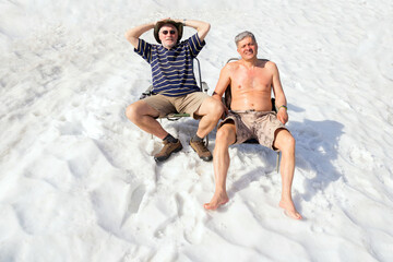sporty mature men sit on deck chairs on the snow and sunbathe