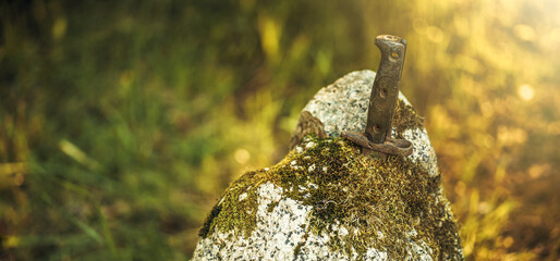 A rusty dagger handle sticks out of a granite stone in a field.Military relics on the battlefield.