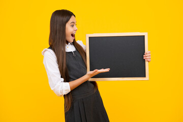 Teenager younf school girl holding school empty blackboard isolated on yellow background. Portrait of a teen female student. Excited face, cheerful emotions of teenager girl.