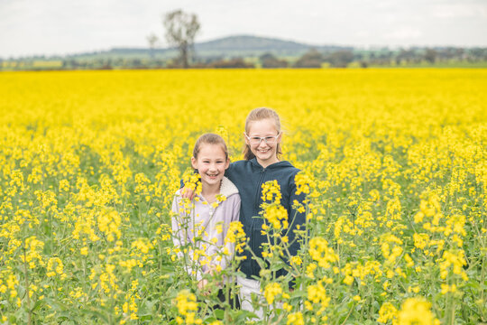 Two Young Sisters Posing In Their Family Canola Field.