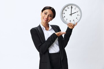Business woman holding a wall clock in a black business suit and glasses showing signals gestures and emotions on a white background, freelancer job online time management