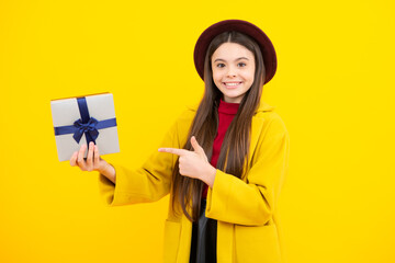 Happy teenager portrait. Smiling girl. Teenager child holding gift box on yellow isolated background. Gift for kids birthday. Autumn holiday.