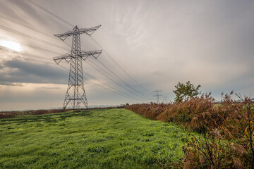 High voltage pylons in a Dutch polder landscape on a cloudy day in autumn. It is still early in the morning, the mist is disappearing and the grass is still wet with the morning dew.
