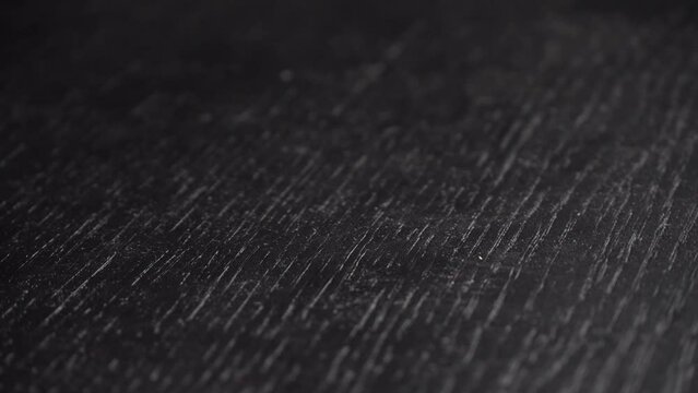 Black table with texture of wood or wood rotates in dim dark room around its axis. Background with space for text. Blank for presentation or video. Ebony texture will reflect light.