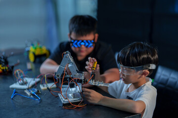 A cute boy constructs metal robot and program it boards microcontrollers on the table STEM education inscription. Programming Mathematics The science Technology DIY workshop at class in the classroom