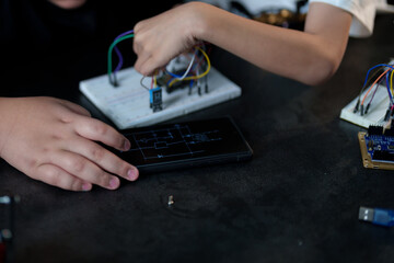 A cute boy constructs metal robot and program it boards microcontrollers on the table STEM education inscription. Programming Mathematics The science Technology DIY workshop at class in the classroom