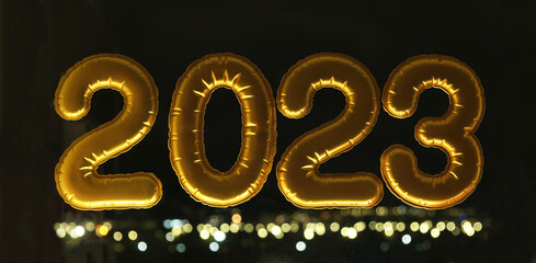 Gold inflatable foil balloons numbers 2023 on the window against the background of the night city, in neon light. New year 2023, christmas. Celebrating Christmas and New Year 2023.