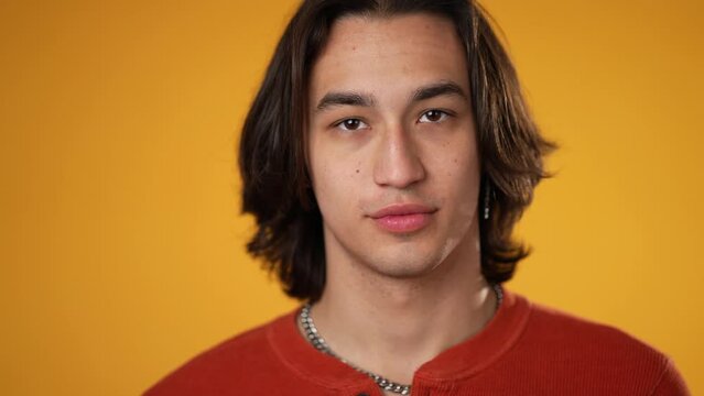 Slow motion portrait nod head yes in agreement by happy smiling Hispanic Latino gender fluid non-binary man isolated on yellow background.