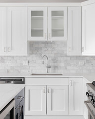 A kitchen sink detail shot with white cabinets and a marble subway tile backsplash.