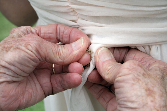 Elderly hands buttoning a dress at the back