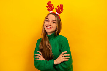 Happy laughing girl wearing green knitted sweater with red Christmas reindeer antlers and looking...