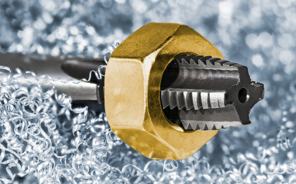 Closeup of gold steel nut on spiral point plug tap in curled swarf heap. Metric screw thread drill bit tool for creating threaded holes on light blue background of metal chips tangle with white bokeh.