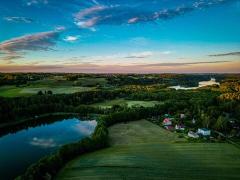 Aerial view of small lake in lush green Ostrzyce village in Poland under colorful sunset clouds