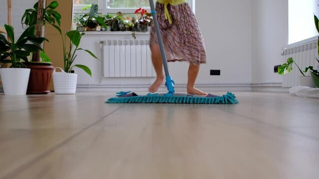 A girl dances with a mop to clean the floor in a new house - general cleaning in an empty room, the joy of moving, help with the housework