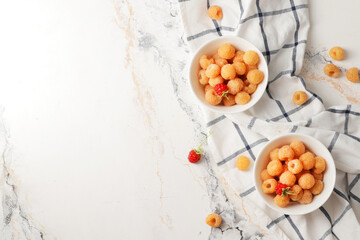 Ripe yellow raspberries in a bowl with a tea towel on a marble background. A bowl full of raspberries. Dessert ingredients.