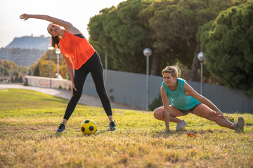 Two 30s years old woman on a training of soccer or European football in amateur team. Yellow ball, sport field with green grass.