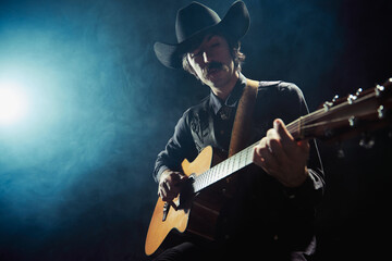 Portrait of man with moustaches in country style clothes playing guitar isolated over dark blue background with smoke