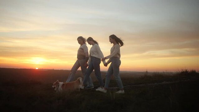 Mother with her daughters and a fluffy corgi are walking on a mountain top at sunset