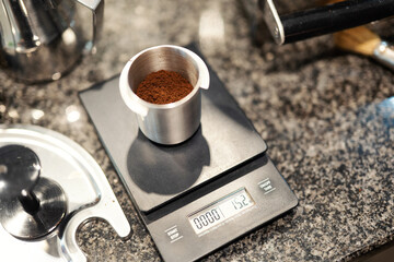 Freshly ground coffee is precisely weighed on a kitchen scale in an aluminum container.