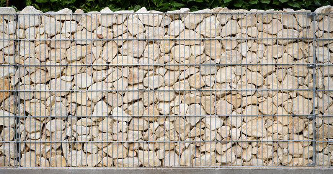 Light beige natural stones are neatly layered in a galvanized gabion wall.