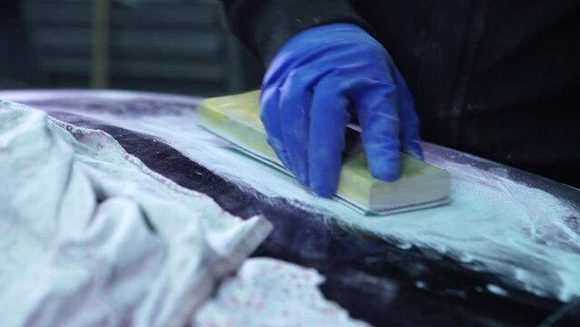 Man worker sanding car hood body element in auto service workshop