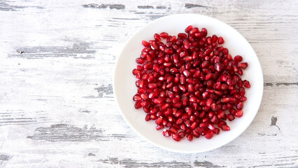 Ripe pomegranate grains in a white plate isolated on a wooden background. Top view, flat lay.
