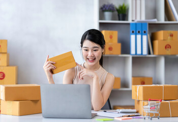 Startup happy Asian woman business owner works with a box at home, prepare parcel delivery SME supply chain, procurement, package box to deliver to customers, Online SME business entrepreneurs ideas