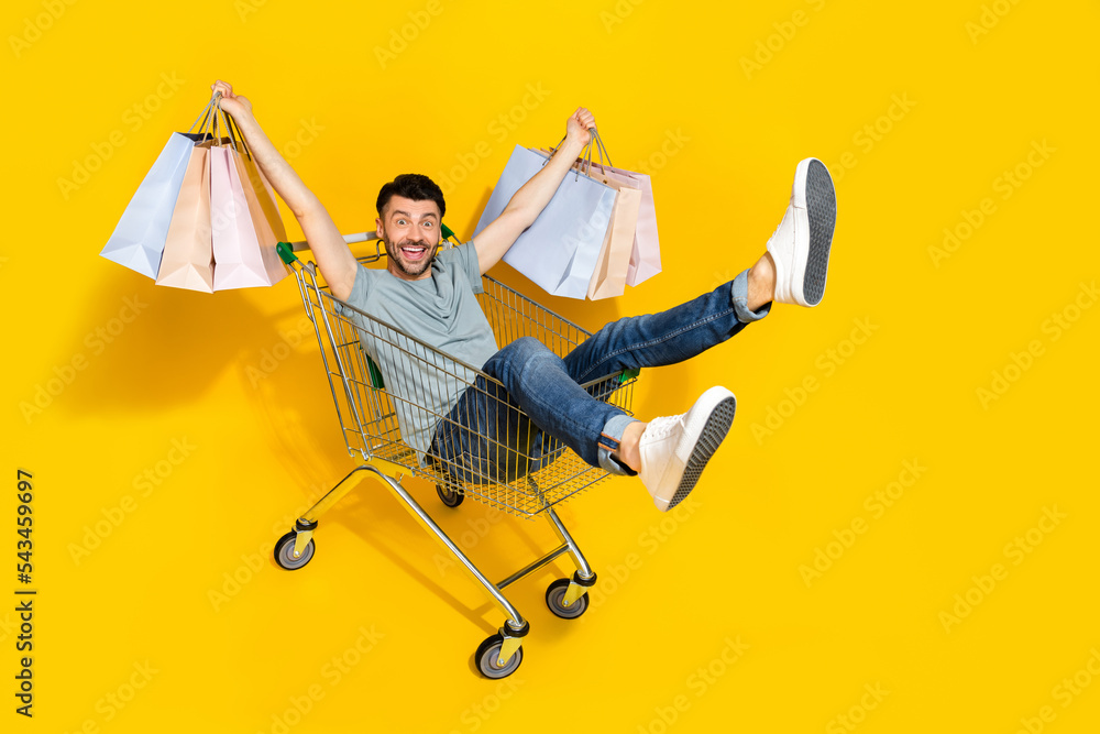 Poster full length photo of overjoyed cheerful person sit market trolley hold shopping bags isolated on yel