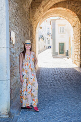 Fototapeta na wymiar Portrait of an attractive tourist woman in old town Wearing stylish long dress, bracelets and straw hat.