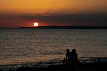 Naklejka na ściany i meble Silhouette of young couple enjoying beautiful sunset at the beach. Romantic moment human relationship