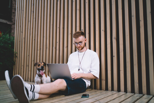 Young man using laptop on wooden bench with smartphone and dog