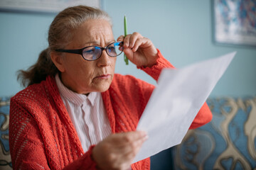 Portrait of a worried, dissatisfied pensioner woman with a utility bill in her hands.