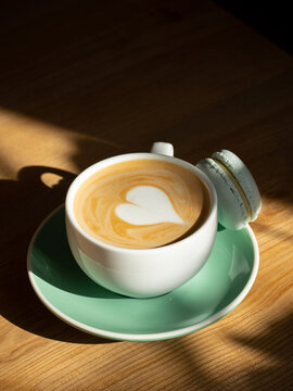 Cup of cappuccino with heart and macaron on a wooden table
