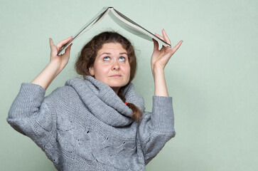 A woman hides under a book, as if under a roof from hostile factors: stress, depression, fear