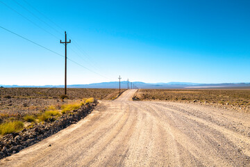 Fototapeta na wymiar Dirt road and the blue sky in the arid wilderness field with electricity poles and cables